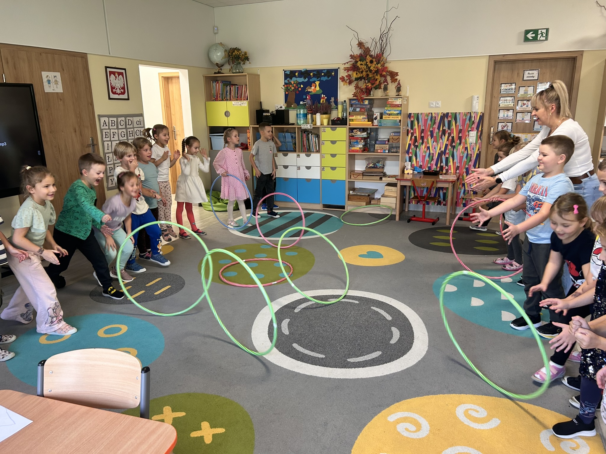 Dzieci toczą do siebie hula-hop.