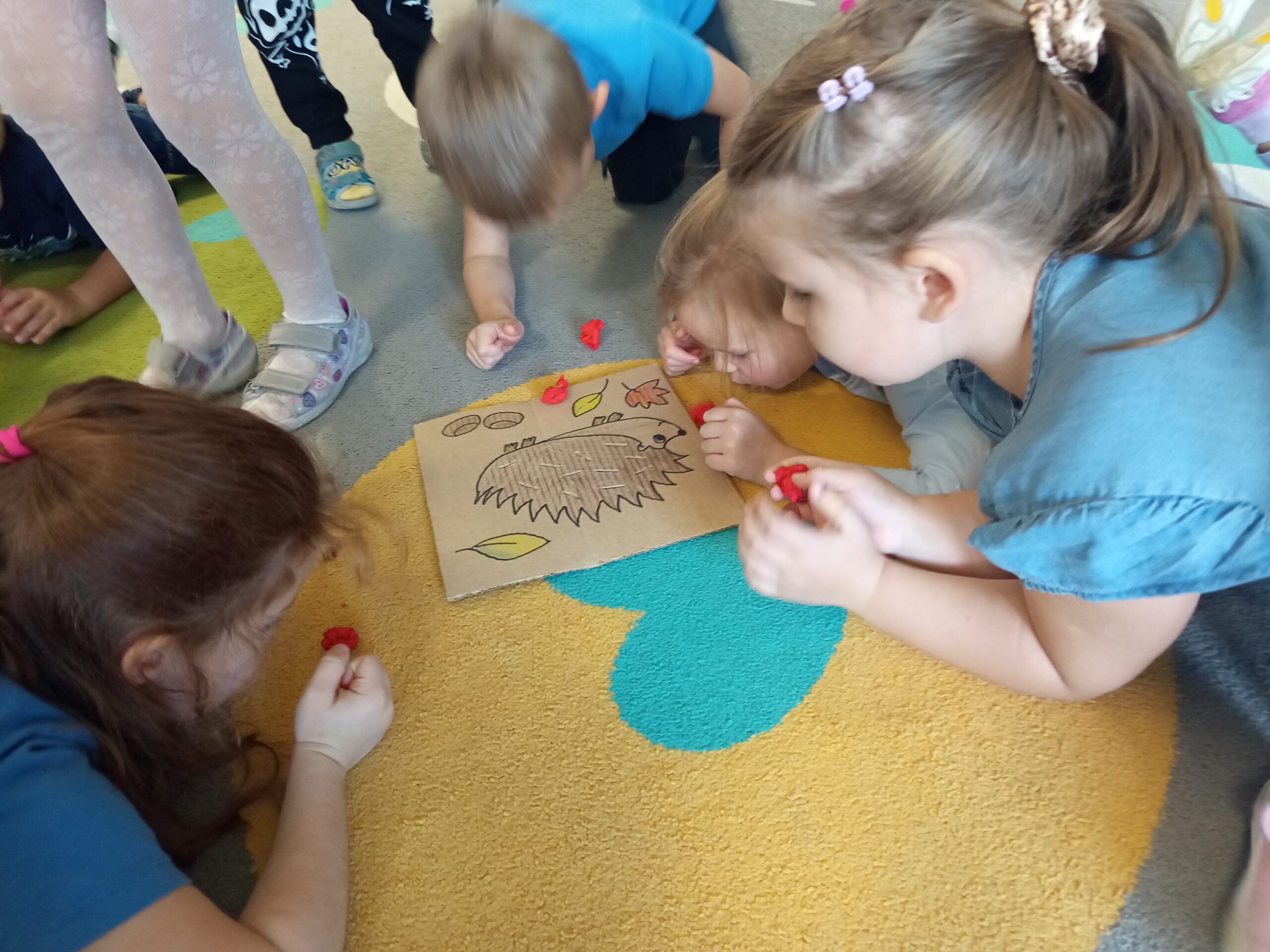 Dzieci wdmuchują bibułkowe jabłuszka na sylwetkę jeżyka.