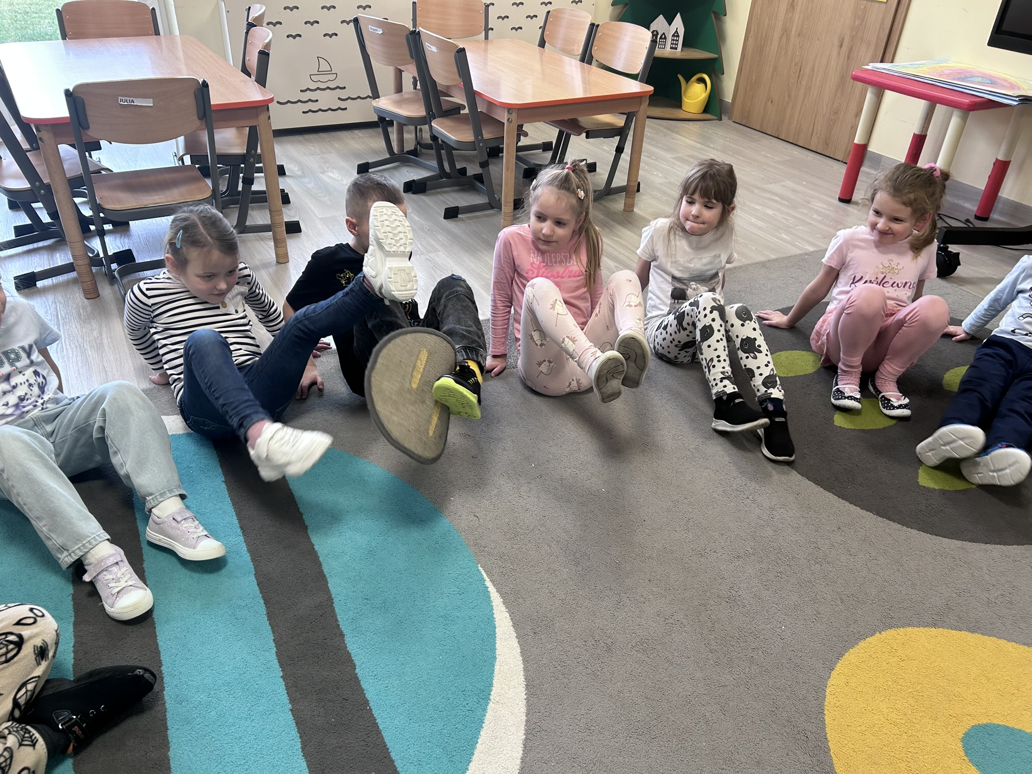 Dzieci podają sobie podkładkę nogami.