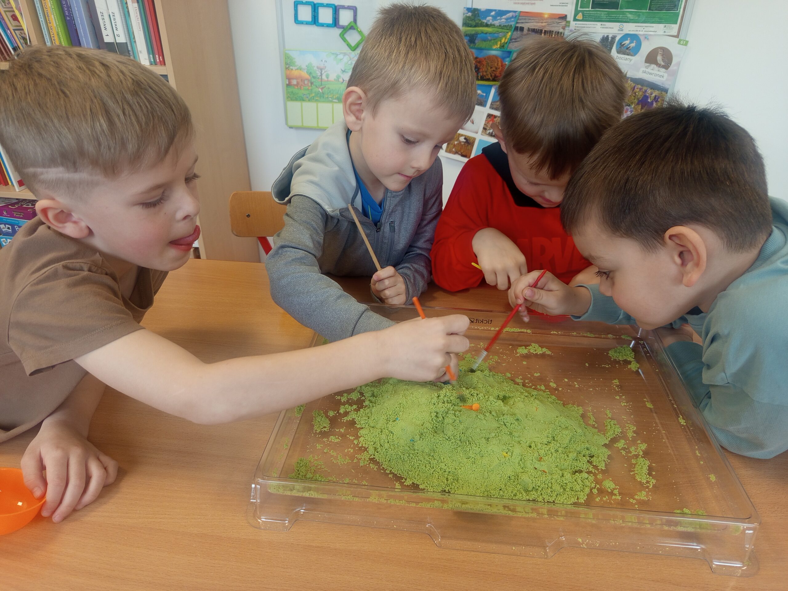 Dzieci szukają dinozaurów w piasku kinetycznym.