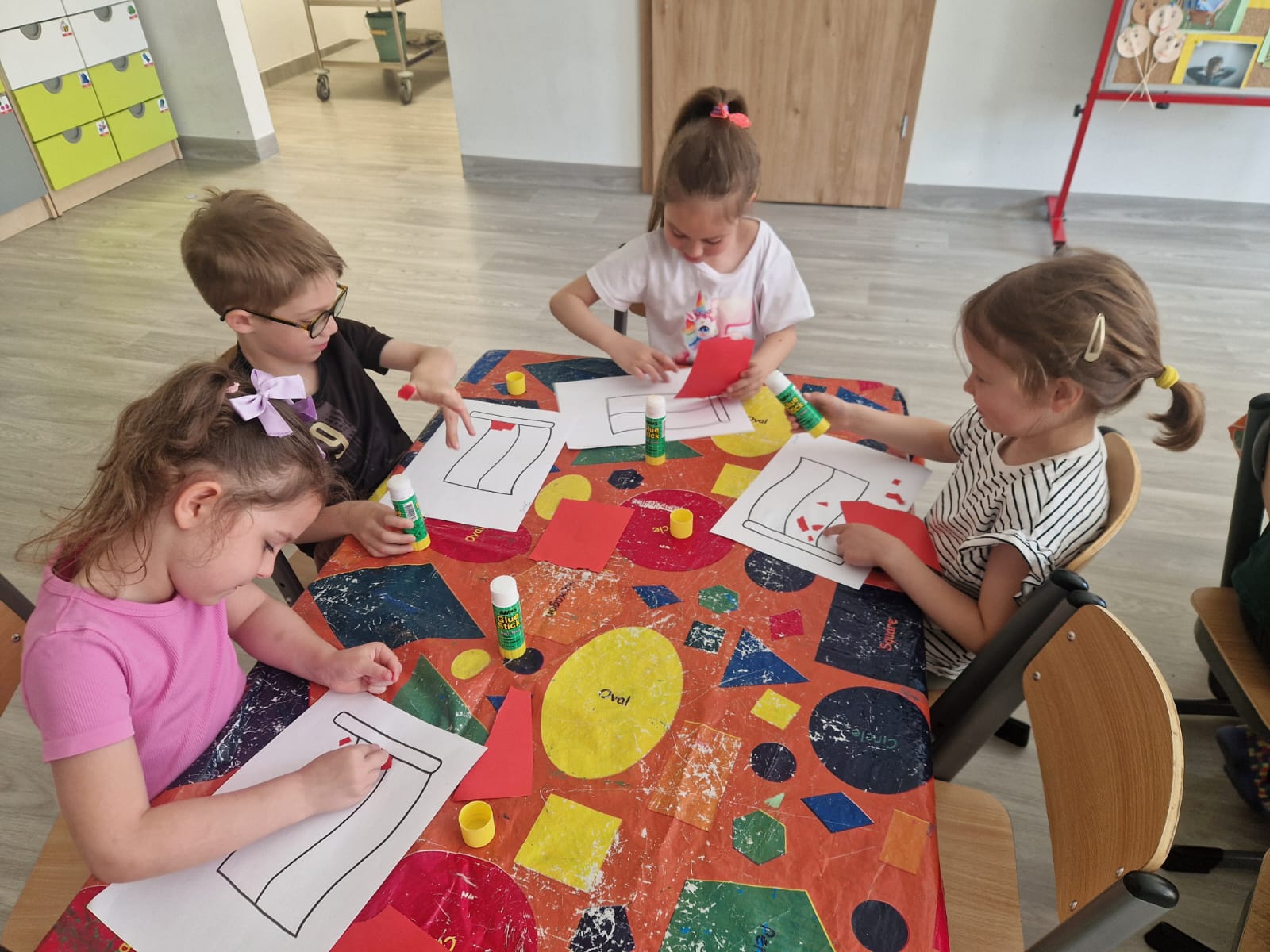 Dzieci pracują przy stolikach wyklejając flagę.