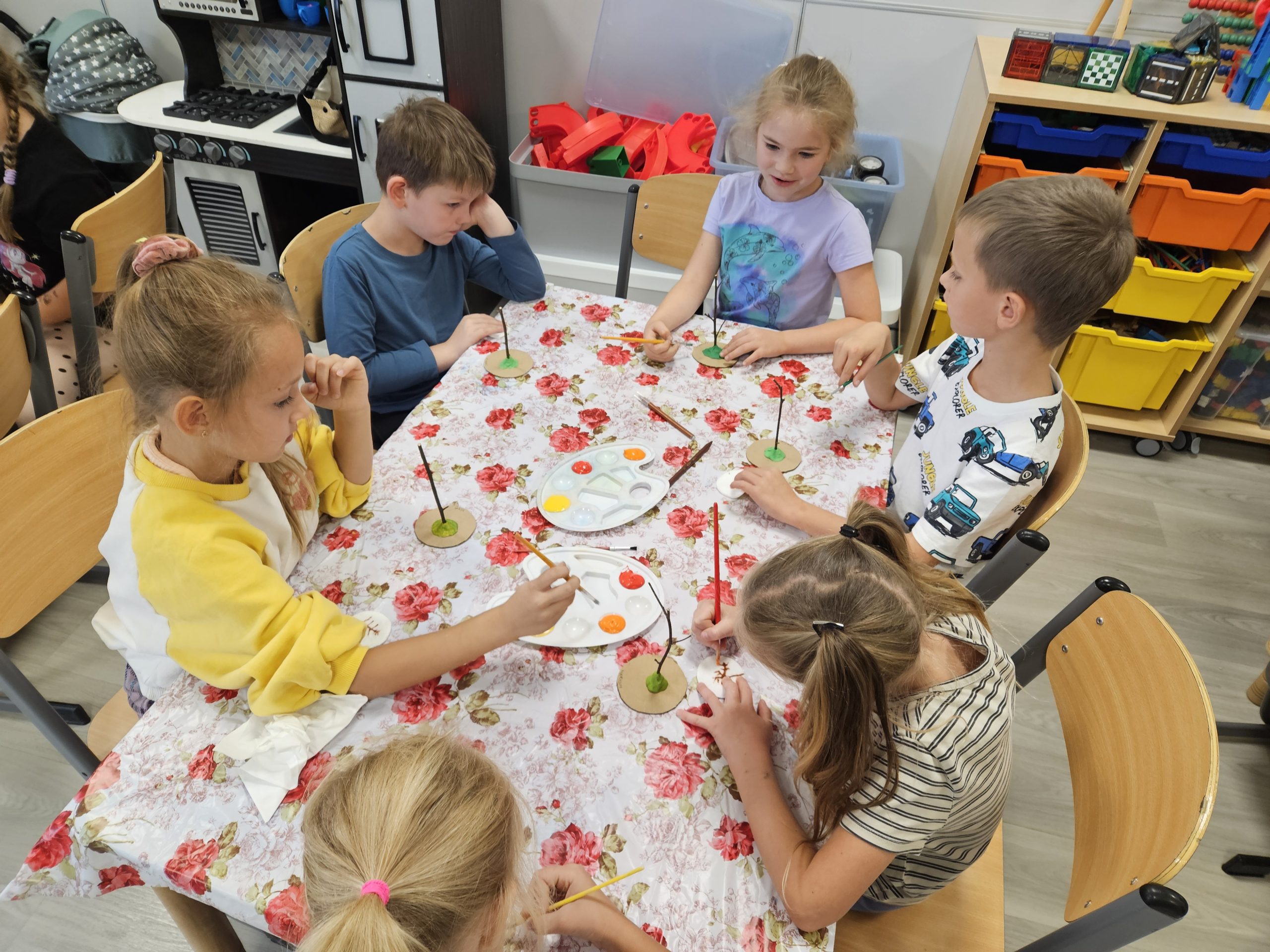 Dzieci malują farbami w kolorach jesieni koronę drzewa na płatkach kosmetycznych.